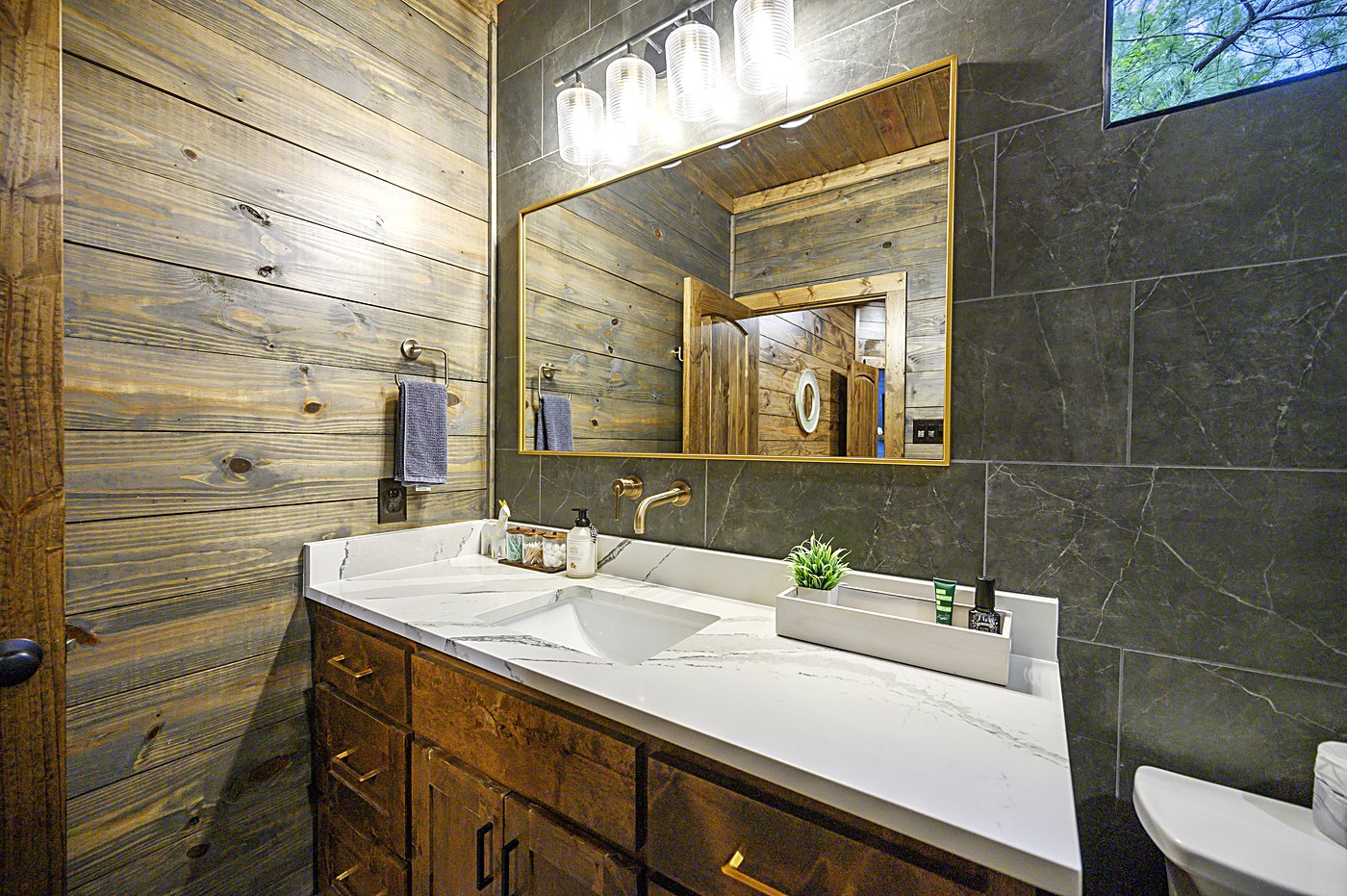 Bathroom with double vanity, dark tile, and brass mirrors